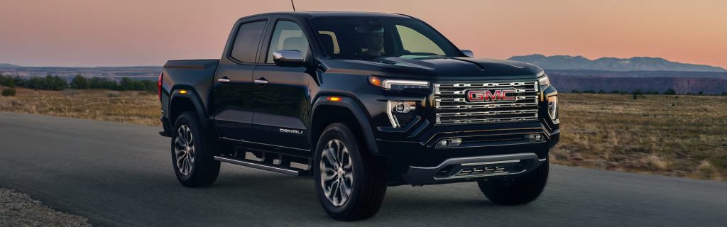Black pickup truck driving on an open road at sunset.