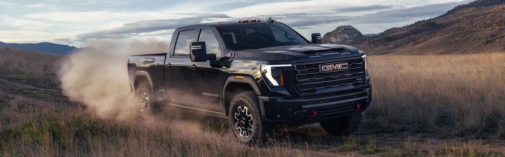 2026 GMC Sierra 2500HD in black driving off-road through dusty terrain
